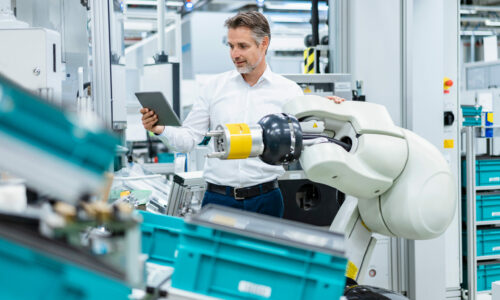 Businessman with tablet at assembly robot in a factory