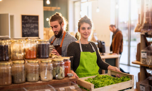 Couple working in a bulk food store the young woman has a crate of salads in her hands