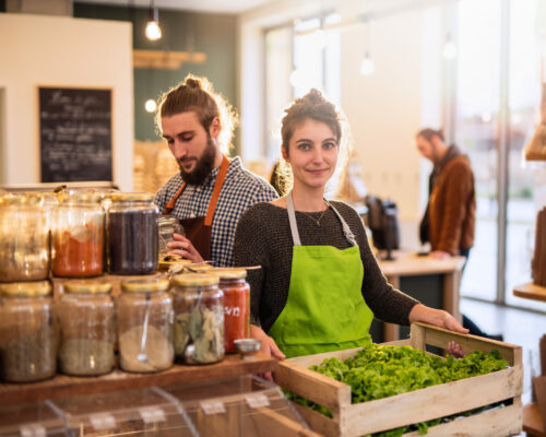 Couple working in a bulk food store the young woman has a crate of salads in her hands