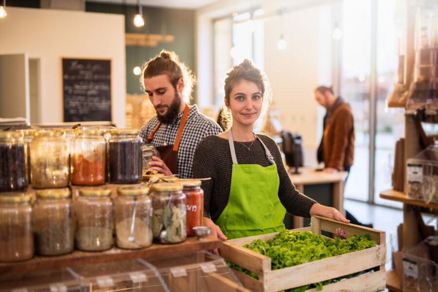Couple working in a bulk food store the young woman has a crate of salads in her hands