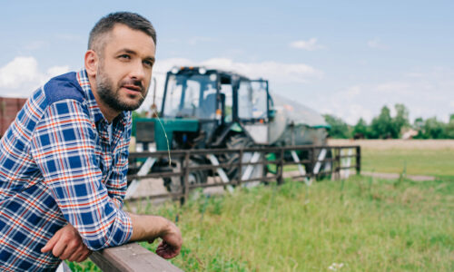 handsome middle aged farmer leaning at fence and looking away at farm
