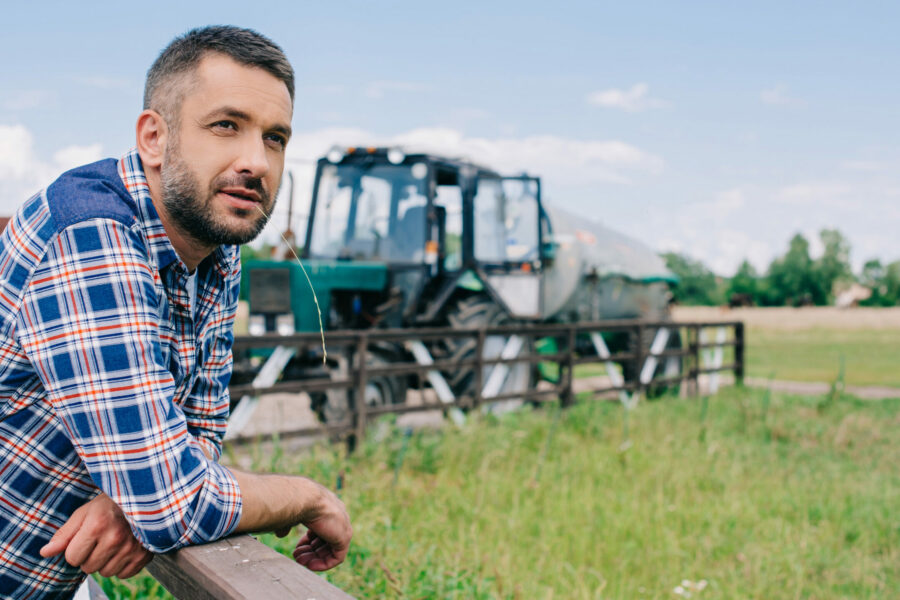 handsome middle aged farmer leaning at fence and looking away at farm