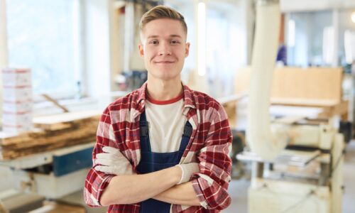 mlady muz v kockovanej koseli a monterkach stojaci v stolarskej dielni