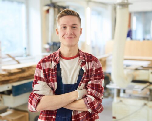 mlady muz v kockovanej koseli a monterkach stojaci v stolarskej dielni