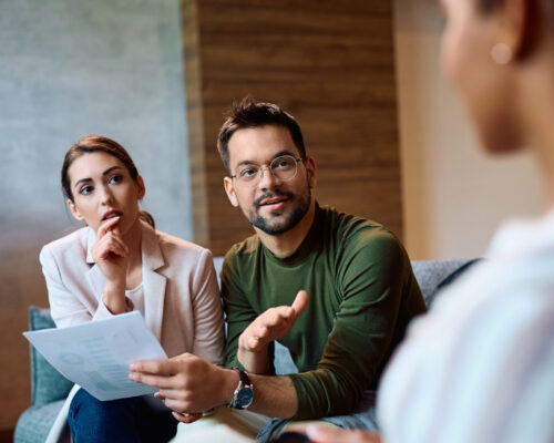 Young couple communicating with insurance agent while analyzing documents during meeting.