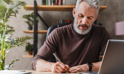 Middle aged businessman in casual clothes making notes in notepad while sitting in his office
